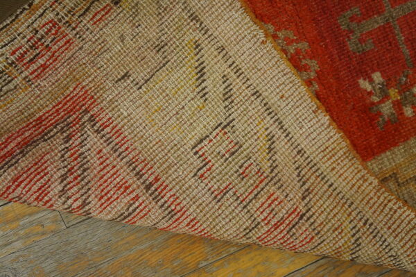 Close-up of a rug's tan woven backing and orange pile resting on distressed wood flooring.