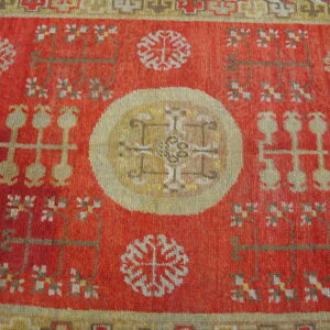 Red rug with a pale gold central medallion and stylized motifs in beige, brown, and white.