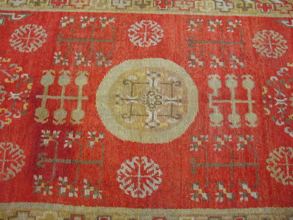 Red rug with a pale gold central medallion and stylized motifs in beige, brown, and white.