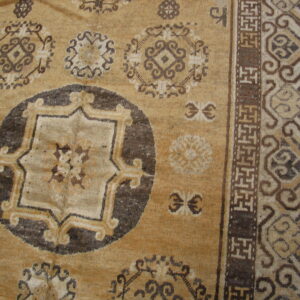 Tan rug featuring dark brown traditional medallions and geometric fretwork borders on wood floor.