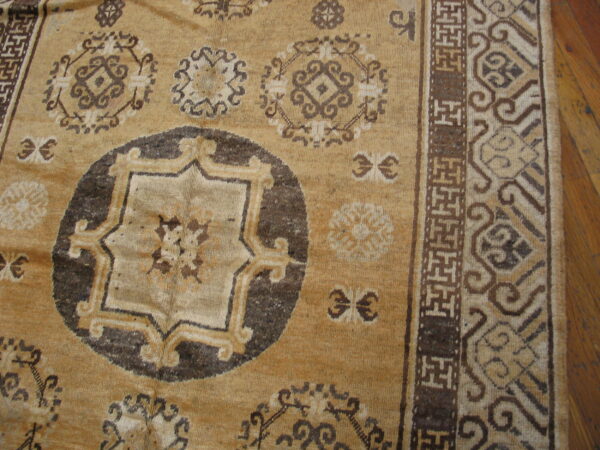 Tan rug featuring dark brown traditional medallions and geometric fretwork borders on wood floor.