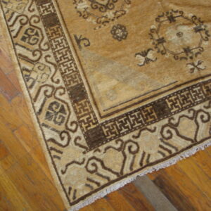 Tan and dark brown geometric rug with a traditional key border lies on light brown hardwood floors.