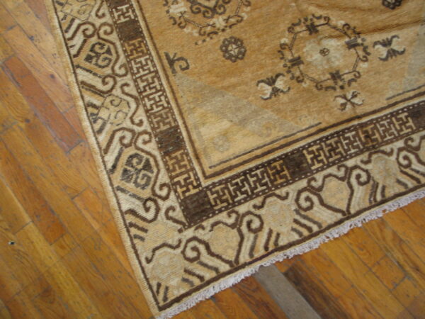 Tan and dark brown geometric rug with a traditional key border lies on light brown hardwood floors.
