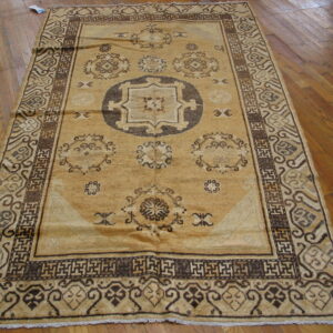 Tan and dark brown geometric pattern rug featuring a central medallion resting on polished wood flooring.