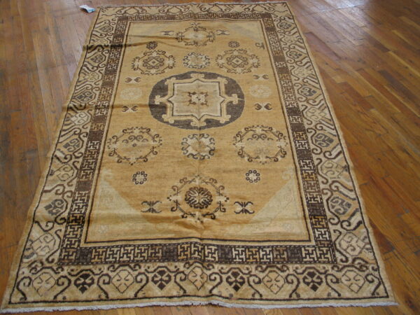 Tan and dark brown geometric pattern rug featuring a central medallion resting on polished wood flooring.