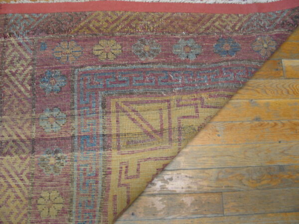 Low-pile rug in maroon, yellow, and blue geometric and floral patterns lays partially folded on hardwood floor.