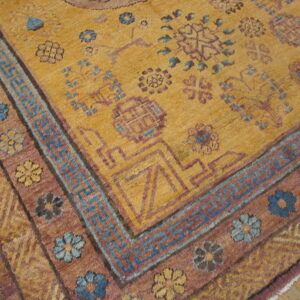 Ochre rug featuring complex geometric borders and floral motifs in purple and light blue on a hardwood floor.