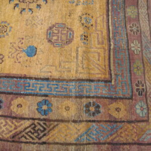 Golden yellow rug detail with stylized purple and blue geometric patterns resting on wood floor.