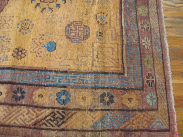 Golden yellow rug detail with stylized purple and blue geometric patterns resting on wood floor.