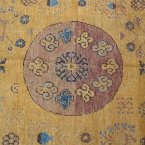Golden yellow low-pile rug showing a round purple center motif with scrolling blue and tan designs.