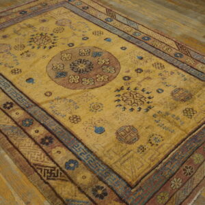 Golden yellow rug with a rose medallion, blue geometric borders, and floral patterns on wood floor.