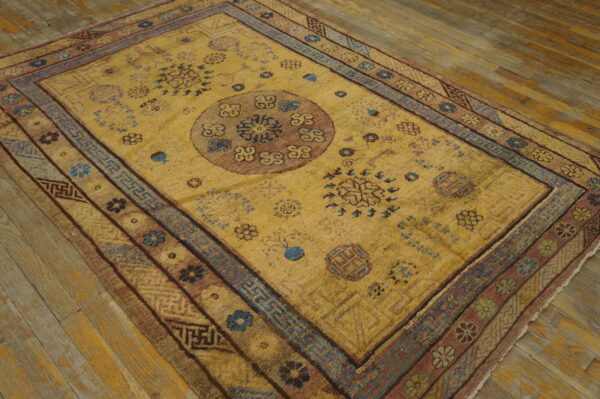 Golden yellow rug with a rose medallion, blue geometric borders, and floral patterns on wood floor.