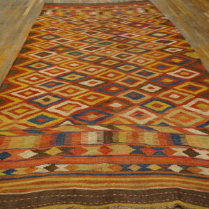 Geometric flatweave runner rug in bright red-orange, yellow, blue, and brown diamonds on plank flooring.