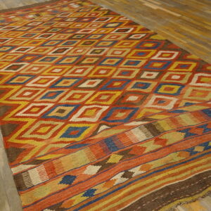 Rust, yellow, blue, and brown flatweave rug with repeating geometric diamonds on wooden planks.