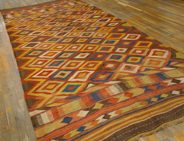 Rust, yellow, blue, and brown flatweave rug with repeating geometric diamonds on wooden planks.