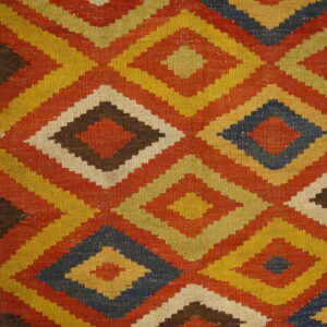 A tightly woven rug displaying stepped, colorful diamonds in yellow, rust, brown, and navy on wooden floorboards.