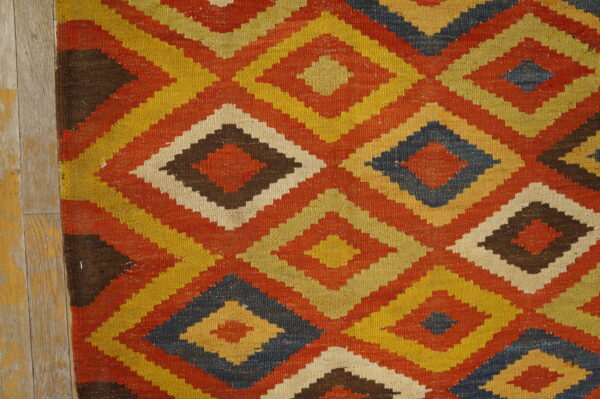 A tightly woven rug displaying stepped, colorful diamonds in yellow, rust, brown, and navy on wooden floorboards.