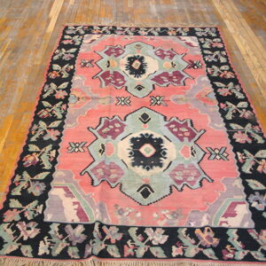 Low pile rug with coral, black, purple, and mint geometric motifs displayed on distressed wood floors.