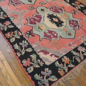 A low-pile rug featuring coral, mint, and maroon geometric patterns with a wide black floral border on wood.