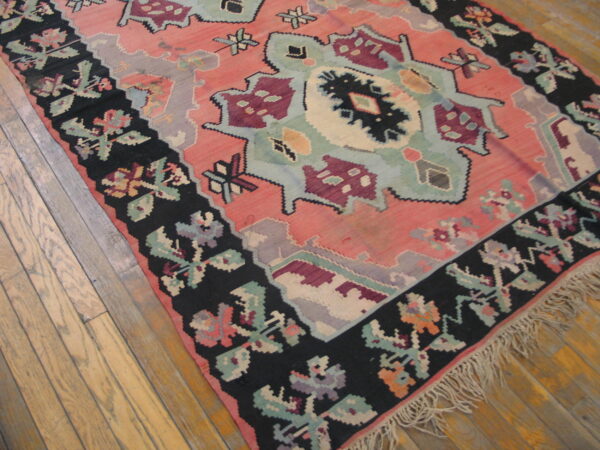 A low-pile rug featuring coral, mint, and maroon geometric patterns with a wide black floral border on wood.