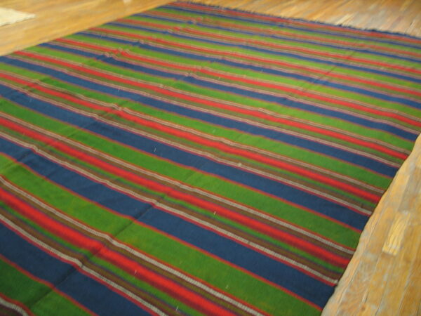 Green, blue, and red striped flatweave rug displayed on light natural wood plank flooring.