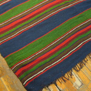 A colorful flatweave rug with wide diagonal stripes in navy, red, green, and maroon lies on wood flooring.