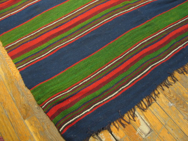 A colorful flatweave rug with wide diagonal stripes in navy, red, green, and maroon lies on wood flooring.