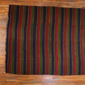 Vertical striped rug in navy, olive green, and red lying flat on a distressed plank wood floor.