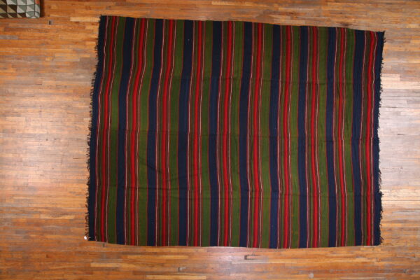 Vertical striped rug in navy, olive green, and red lying flat on a distressed plank wood floor.