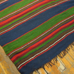 Close-up of a striped flatweave rug in blue, green, red, and maroon on worn wood plank flooring.