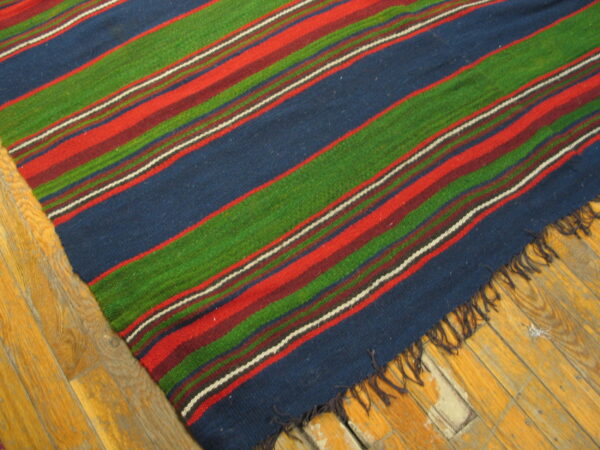 Close-up of a striped flatweave rug in blue, green, red, and maroon on worn wood plank flooring.