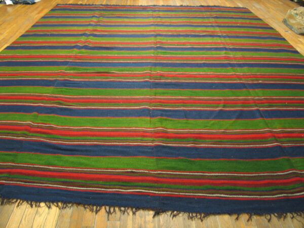 A low-pile rug featuring wide horizontal stripes in blue, green, and red rests on a wood plank floor.