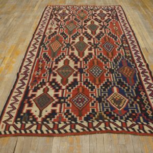 Low pile rug with red, cream, navy, and black geometric patterns on worn light hardwood flooring.