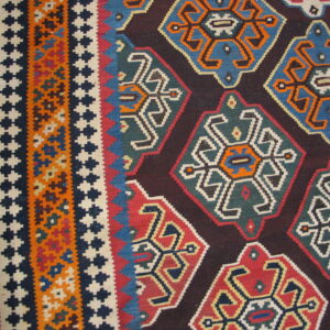 Geometric flatweave rug in red, blue, teal, orange, and dark brown resting on a light wood floor.