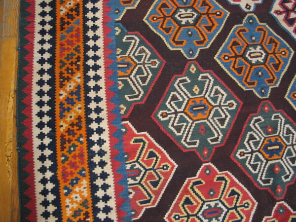 Geometric flatweave rug in red, blue, teal, orange, and dark brown resting on a light wood floor.