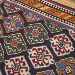 Flatwoven rug with large, colorful geometric medallions and striped borders sits on a hardwood floor.