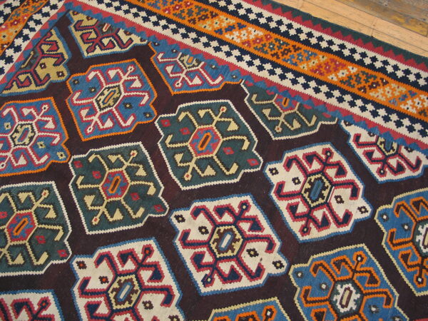 Flatwoven rug with large, colorful geometric medallions and striped borders sits on a hardwood floor.