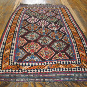 Flat-weave rug with dark red field, bright geometric medallions, wide orange borders, and wood flooring.