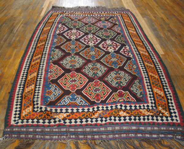Flat-weave rug with dark red field, bright geometric medallions, wide orange borders, and wood flooring.
