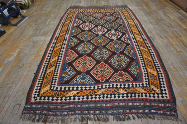 Dark geometric rug with red, blue, gold, and white stylized motifs on distressed wood floors.