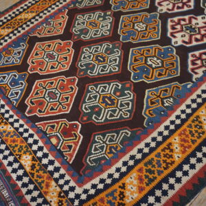 Geometric flat-weave rug with multicolored medallions, striped borders, and tassels shown on rustic wood flooring.