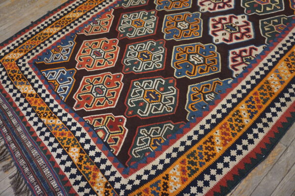 Geometric flat-weave rug with multicolored medallions, striped borders, and tassels shown on rustic wood flooring.