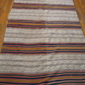 Flatweave rug featuring colorful horizontal stripes and patterned white bands on a wood plank floor.