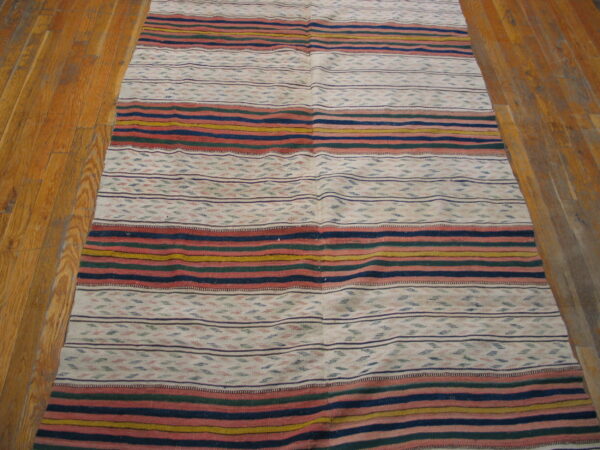 Flatweave rug featuring colorful horizontal stripes and patterned white bands on a wood plank floor.