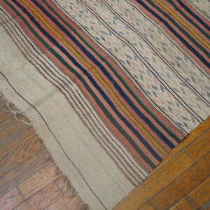A flatwoven rug with colorful stripes and patterned beige panels lays over worn wooden floorboards.