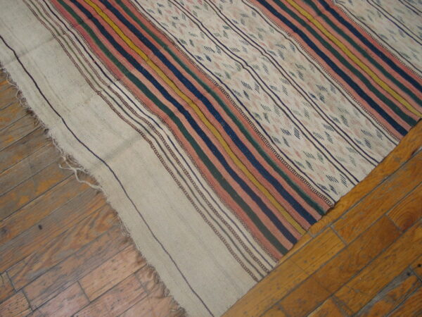 A flatwoven rug with colorful stripes and patterned beige panels lays over worn wooden floorboards.