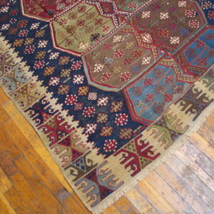 Patchwork geometric flatweave rug featuring navy, olive, red, and tan panels on wood planks.