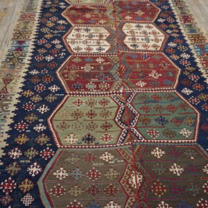 Geometric flat-weave rug with navy blue borders and large hexagonal panels in red, green, and white on wood flooring.