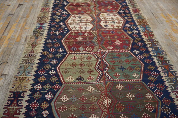 Geometric flat-weave rug with navy blue borders and large hexagonal panels in red, green, and white on wood flooring.