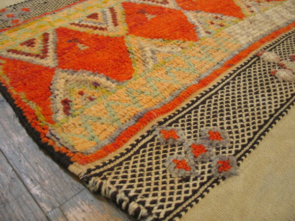 Shaggy orange and pastel geometric rug detail on gray wood features a contrasting dark diamond-patterned border.